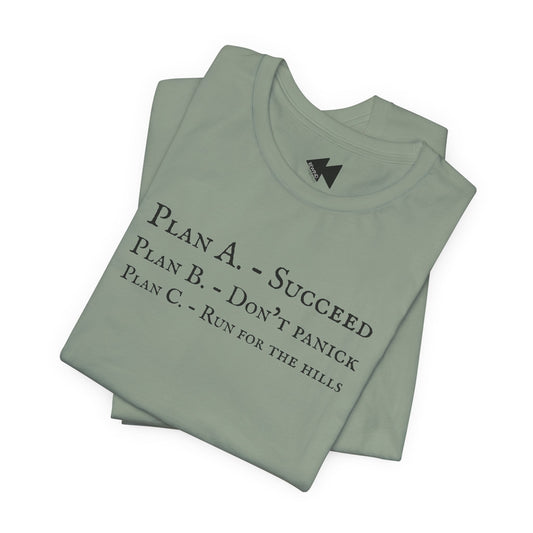 A sage folded short-sleeve crewneck t-shirt with black printed text on the front reading 'PLAN A. - SUCCEED PLAN B. - DON'T PANICK PLAN C. RUN FOR THE HILLS'