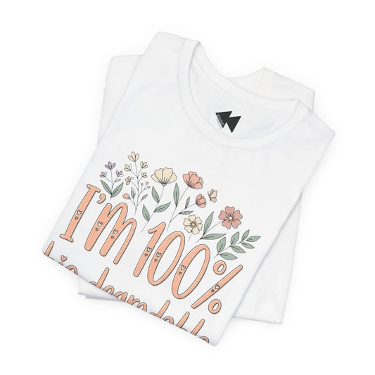 A folded white t-shirt that reads 'I'm 100% bio-degradable' in peach-colored lettering, decorated with small pastel flowers above the text.