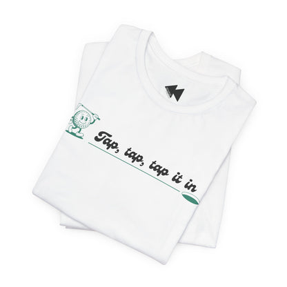 A folded white t-shirt with a green and black graphic on the chest that reads 'Tap, tap, tap it in' next to a cartoon character, shown on a clean white background.