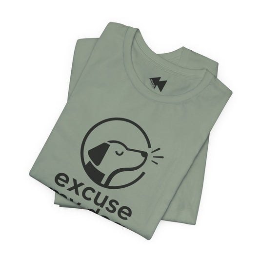 A folded sage green t-shirt with a black graphic of a dog inside a circle and the word 'excuse' printed below, displayed on a clean white background.