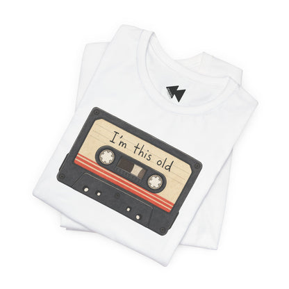 A folded white t-shirt featuring a graphic of a retro cassette tape with the text 'I'm this old' written on it, set against a plain white background.