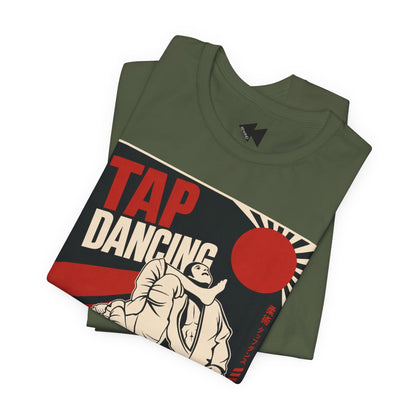 An olive green folded t-shirt with a vintage-style 'TAP DANCING' graphic print on the front, featuring a BJJ fighters illustration and a red rising sun, set against a plain white background.