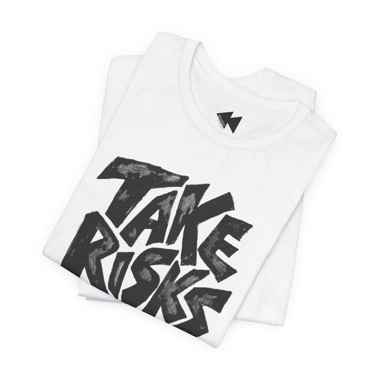 A folded white t-shirt with a large black graphic print reading 'TAKE RISKS' in a bold, hand-drawn style. A small black lightning bolt logo is visible inside the collar.