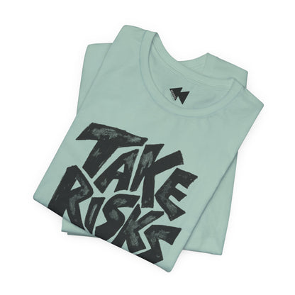 A folded mint green t-shirt with a bold black graphic reading 'TAKE RISKS' across the front, displayed on a clean white background.