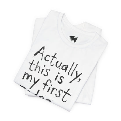 A folded white t-shirt with black handwritten-style text reading 'Actually, this is my first...' on a plain white background.
