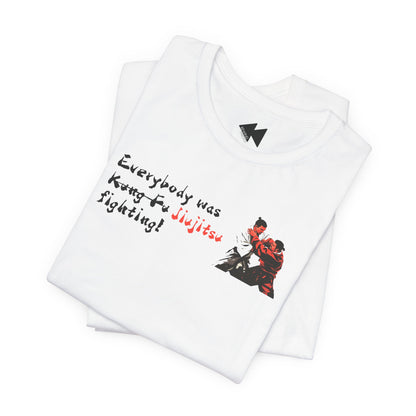A folded white t-shirt with a graphic print on the front. The print features the text 'Everybody was Jujitsu!' in black and red script alongside an illustration of two martial artists in a grappling stance.
