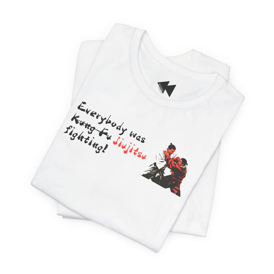 A folded white t-shirt with a graphic print on the front. The print features the text 'Everybody was Jujitsu!' in black and red script alongside an illustration of two martial artists in a grappling stance.