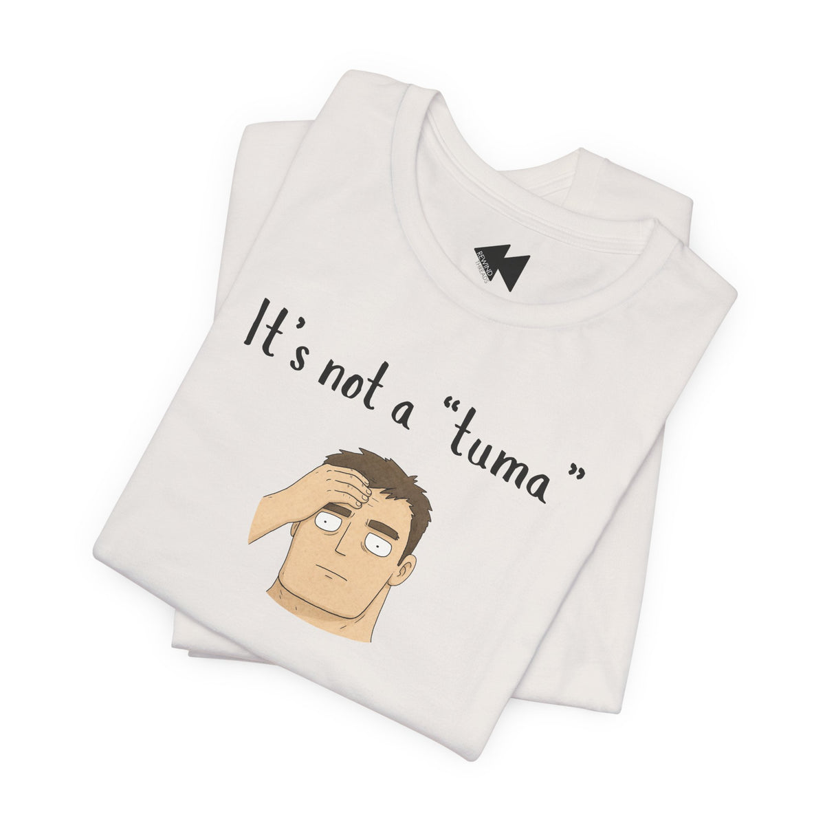 A folded light beige t-shirt with a graphic print that reads 'It's not a "tuma"' above an illustration of a confused man scratching his head. The shirt features a black geometric logo inside the collar.