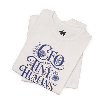 A folded white t-shirt with a blue graphic print that reads 'CEO of TINY HUMANS' in an ornate script with floral details, set against a plain white background.