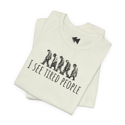 A folded off-white t-shirt with a black graphic of six walking figures and the text 'I SEE TIRED PEOPLE' printed on the front, set against a plain white background.