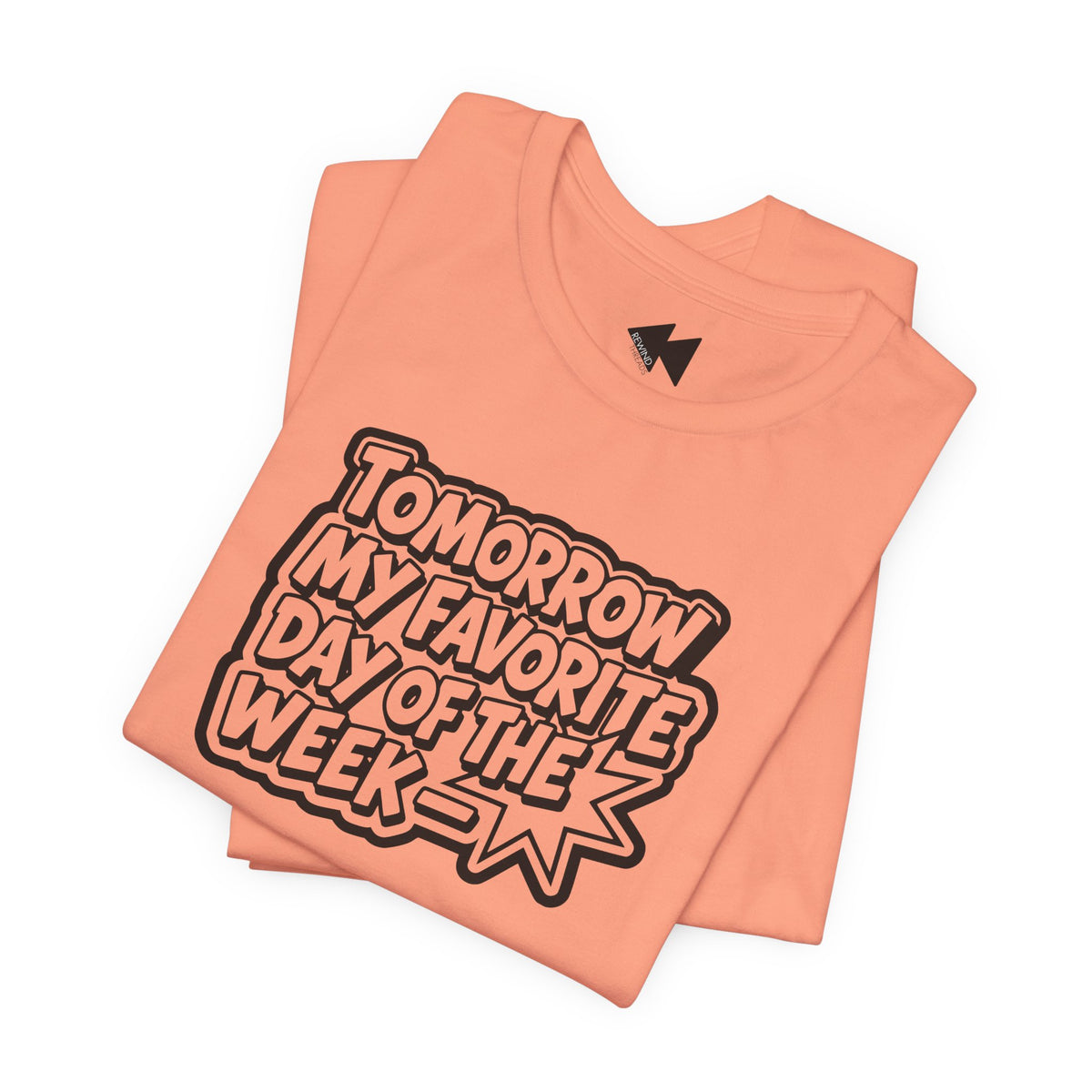 A folded peach-colored t-shirt with a bold graphic reading 'TOMORROW MY FAVORITE DAY OF THE WEEK' in black and white bubble letters, set against a plain white background.