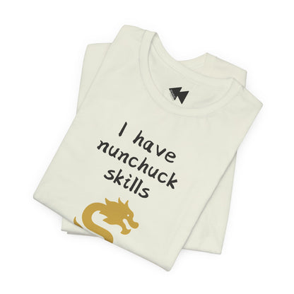 A folded off-white t-shirt with the text 'I have nunchuck skills' in black handwritten-style font and a gold dragon graphic, shown on a plain white background.