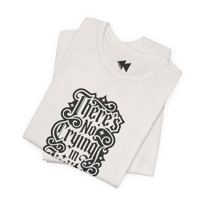 A folded light beige short-sleeve T-shirt with a black gothic-style graphic text print reading 'There's No Crying in JiuJitsu' on the front, displayed against a clean white background.