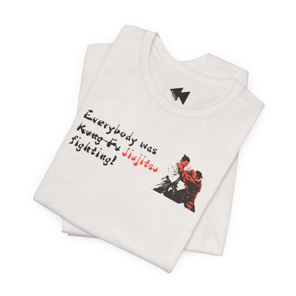 A folded white t-shirt with a graphic print on the front. The print features the text 'Everybody was Jiujitsu Fighting!' in black and red script, alongside an illustration of two martial artists in a black-and-red gi.