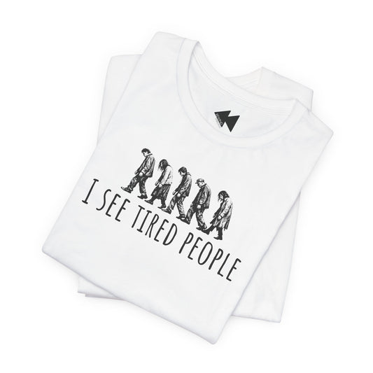 A folded white t-shirt with a black graphic print showing a line of walking figures and the text 'I SEE TIRED PEOPLE'. A small black lightning bolt logo is printed inside the collar.