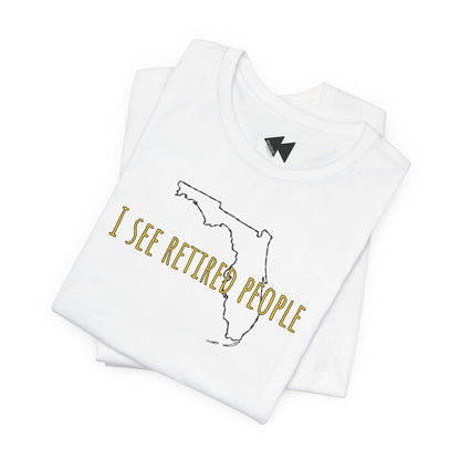 A folded white t-shirt with a graphic print featuring the outline of the state of Florida and the text 'I SEE RETIRED PEOPLE' in gold lettering, displayed on a clean white background.