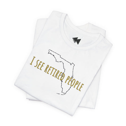 A folded white t-shirt with a graphic print featuring the outline of the state of Florida and the text 'I SEE RETIRED PEOPLE' in gold lettering, displayed on a clean white background.