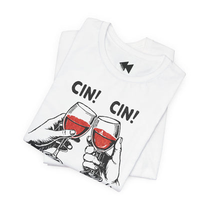 A folded white t-shirt with a graphic print of two hands clinking wine glasses filled with red wine, with the text 'CIN! CIN!' printed above. A small black geometric logo is visible inside the collar.