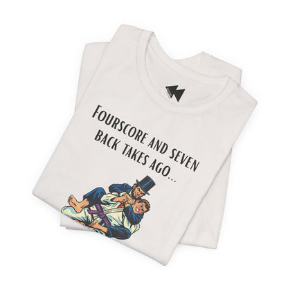 A folded light beige t-shirt with a black graphic print that reads 'Fourscore and Seven Back Takes Ago.