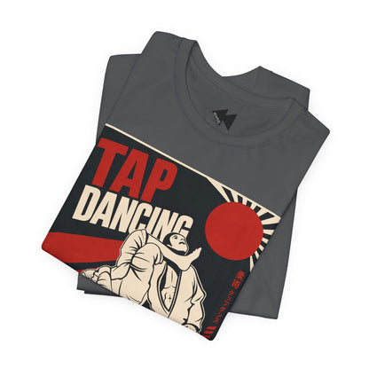 A folded dark gray T-shirt with a vintage-style 'TAP DANCING' graphic in red, white, and beige, featuring an illustration of two BJJ fighters and a rising sun, shown on a plain white background.