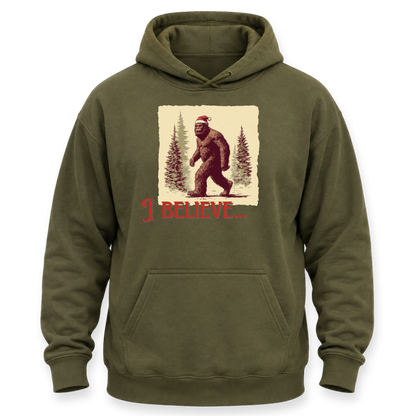 An olive green pullover hoodie with a front graphic of Bigfoot wearing a Santa hat in a snowy forest, with the text 'I BELIEVE.