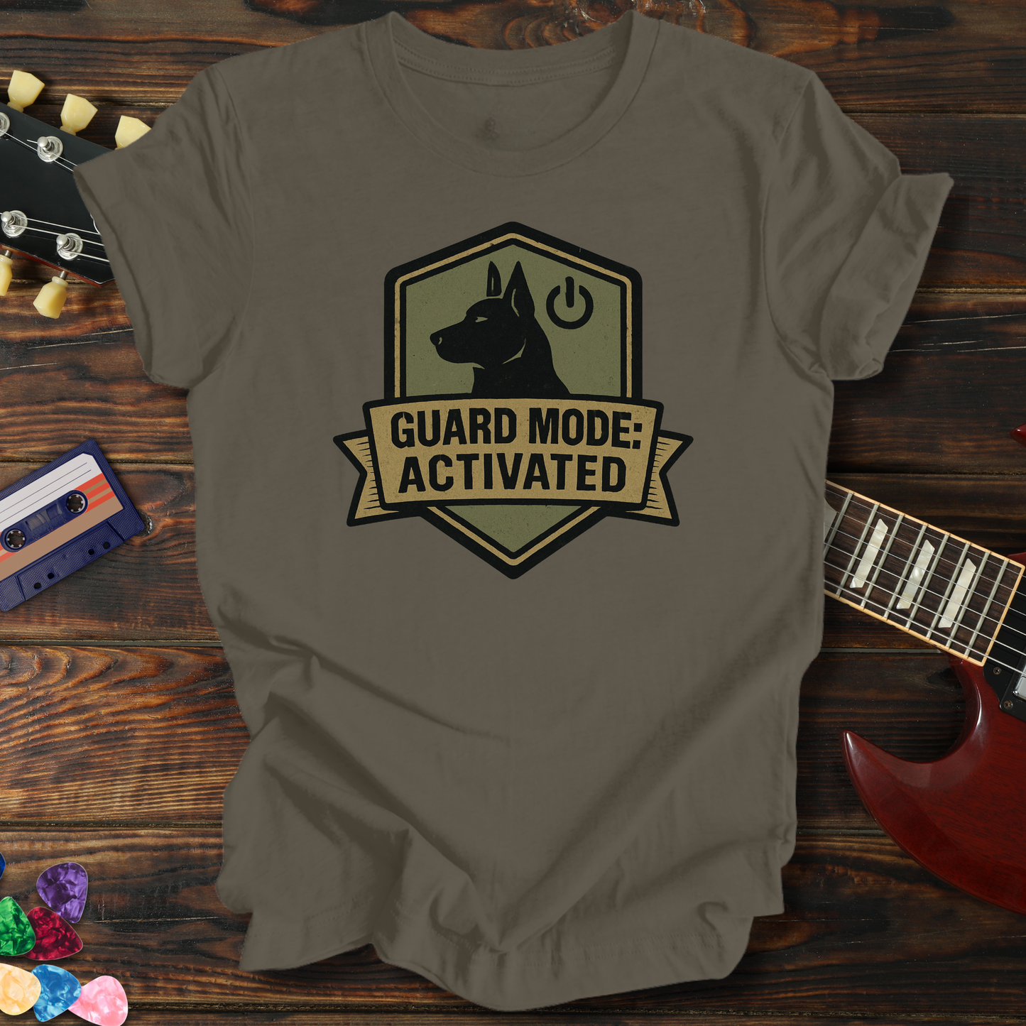 Brown t-shirt with 'Guard Mode: Activated' graphic on a wooden surface with a guitar and cassette tape.