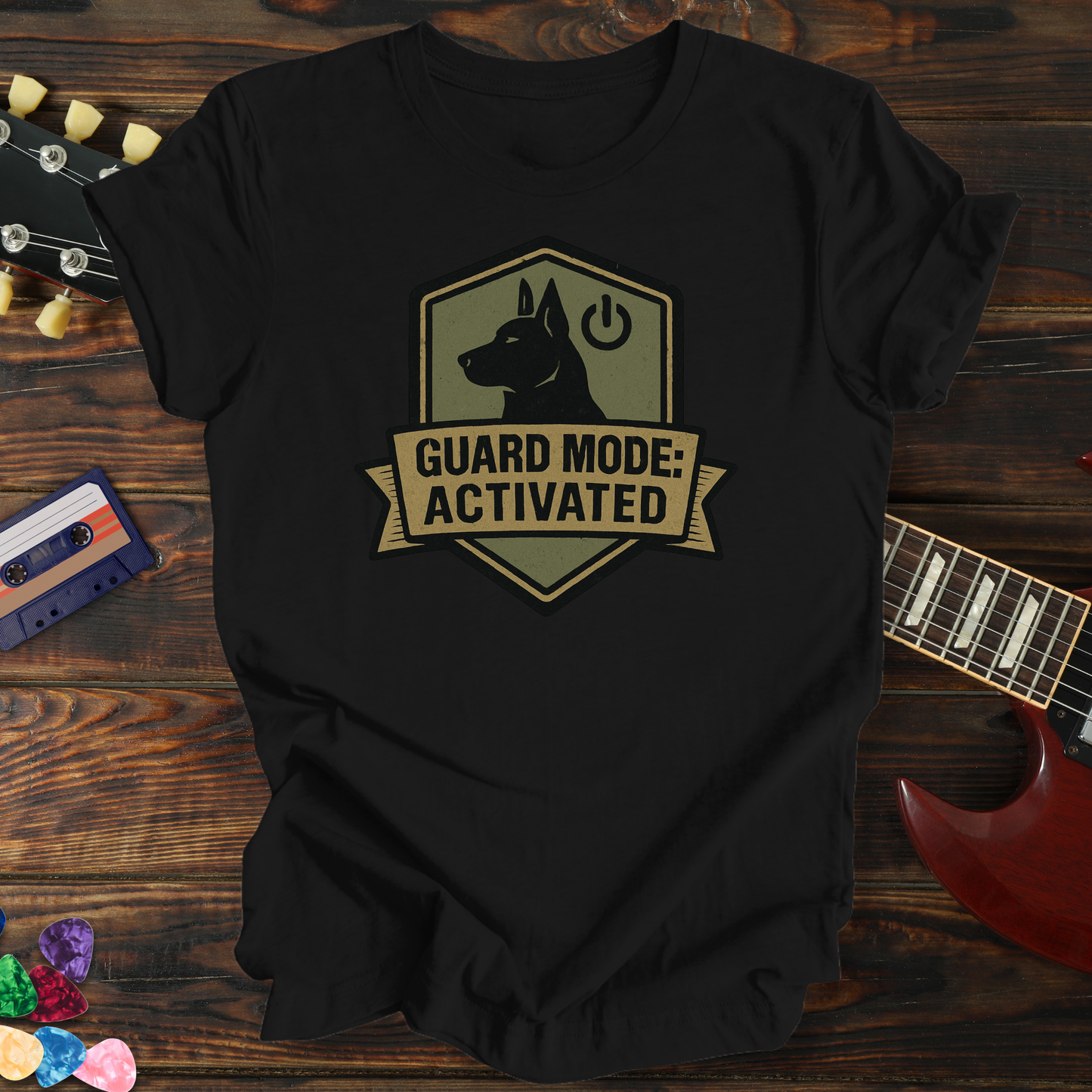 Black t-shirt with 'Guard Mode: Activated' graphic on a wooden surface with guitar and cassette tape.