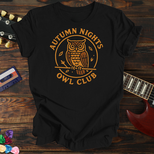 Black t-shirt with 'Autumn Nights Owl Club' design on a wooden surface with a guitar and cassette tape.