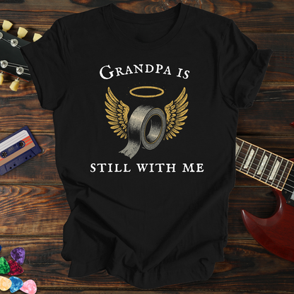 Black t-shirt with 'Grandpa is still with me' design on a wooden surface with a guitar and cassette tape.