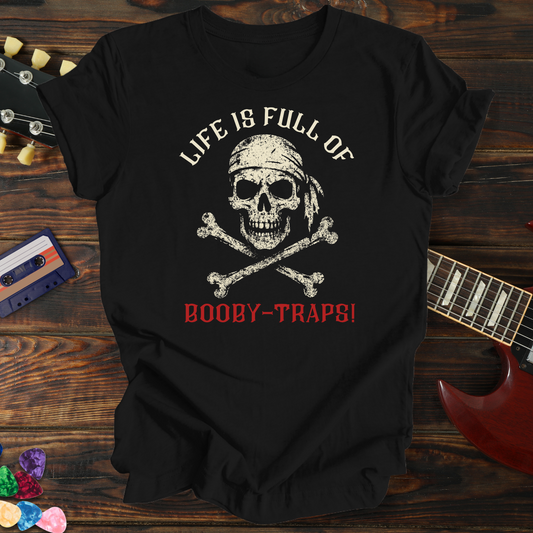 Black t-shirt with skull and crossbones design on a wooden surface with guitar and cassette tape.