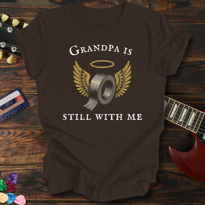 Brown t-shirt with 'Grandpa is still with me' graphic on a wooden surface with a guitar and cassette tape.