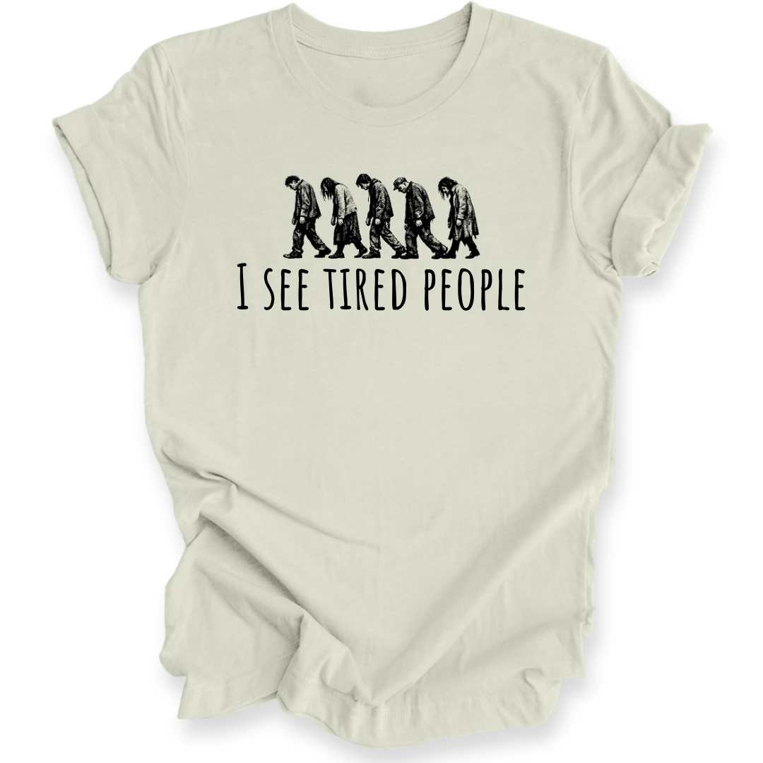 A light beige crewneck t-shirt with a black graphic of five progressively slouching figures and the text 'I SEE TIRED PEOPLE' printed on the front, displayed against a clean white background.