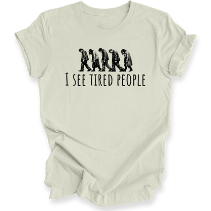A light beige crewneck t-shirt with a black graphic of five progressively slouching figures and the text 'I SEE TIRED PEOPLE' printed on the front, displayed against a clean white background.