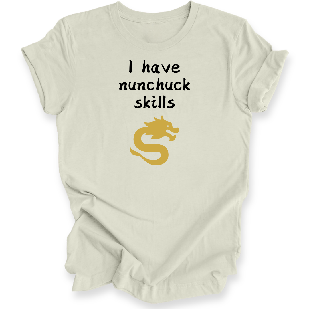 A light beige short-sleeve t-shirt with a graphic print that reads 'I have nunchuck skills' in black text above a gold dragon illustration, displayed on a clean white background.