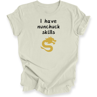 A light beige short-sleeve t-shirt with a graphic print that reads 'I have nunchuck skills' in black text above a gold dragon illustration, displayed on a clean white background.