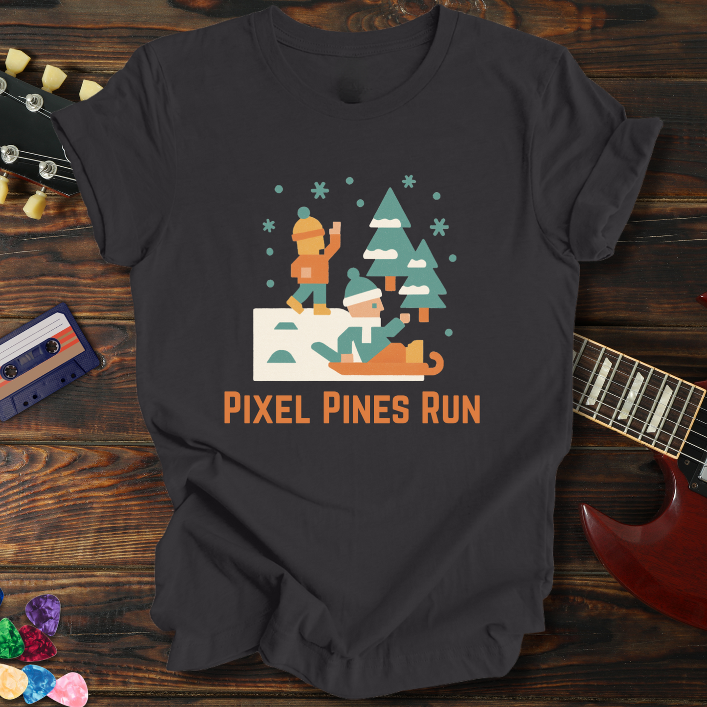 Black t-shirt with 'Pixel Pines Run' graphic on a wooden surface with a guitar and cassette tape.