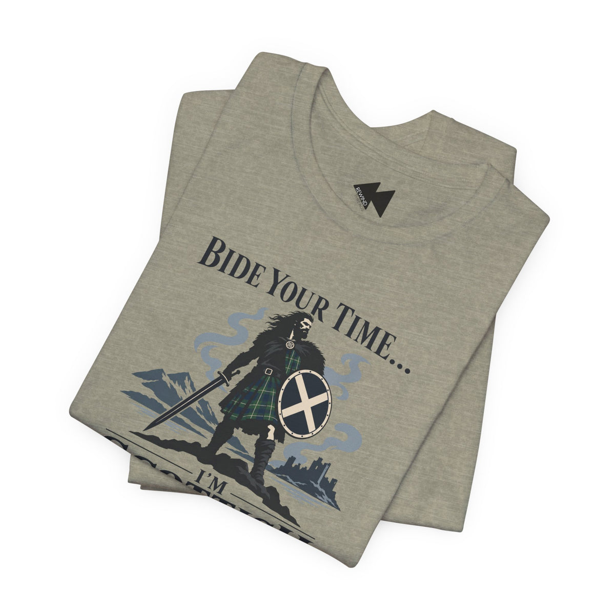 A folded heather gray t-shirt featuring a graphic of a Scottish warrior in a kilt with a sword and shield, accompanied by the text 'BIDE YOUR TIME.