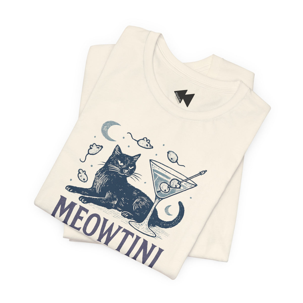 An off-white folded t-shirt featuring a dark blue graphic of a cat sitting next to a martini glass with mice and moons, and the word 'MEOWTINI' printed below.