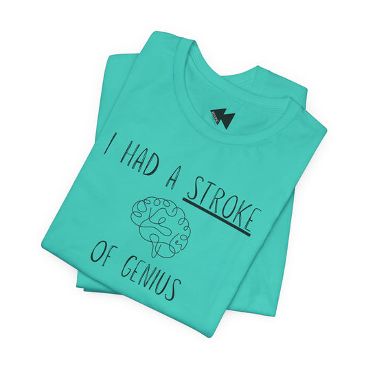 A folded mint green t-shirt with a black graphic print that reads 'I HAD A STROKE OF GENIUS' surrounding a simple line drawing of a brain. The shirt is displayed on a clean white background.