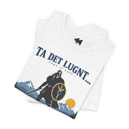 A folded white t-shirt with a Viking-themed graphic print featuring a silhouette of a warrior with a shield, mountains, and the text 'TA DET LUGNT.
