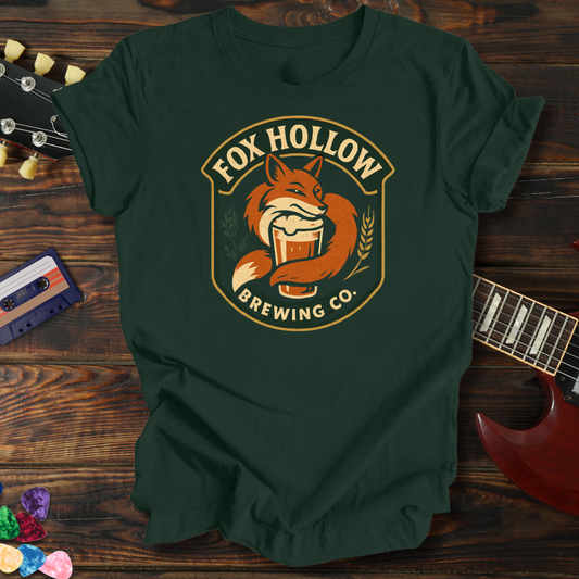Green t-shirt with Fox Hollow Brewing Co. logo on a wooden surface with a guitar and cassette tape.
