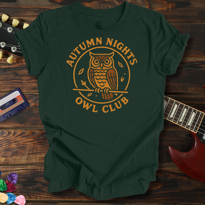 Green t-shirt with 'Autumn Nights Owl Club' design on a wooden surface with a guitar and cassette tape.