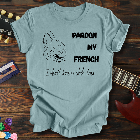 Light blue t-shirt with dog graphic and text on a wooden surface with a guitar and cassette tape.