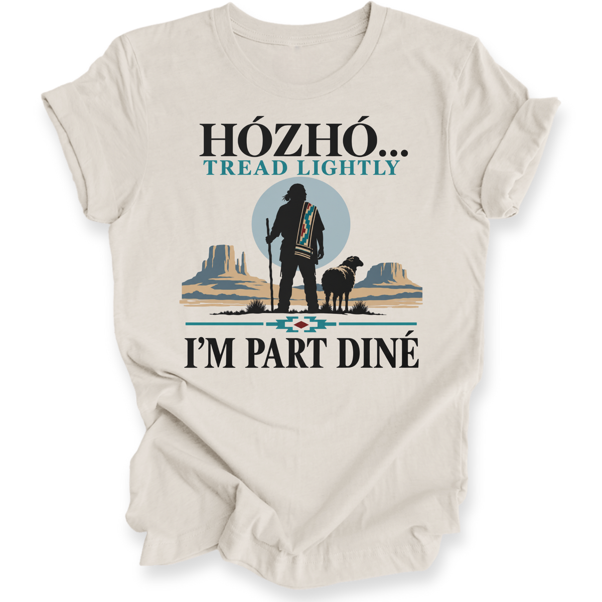 A beige short-sleeve t-shirt with a graphic print on the front. The graphic features a silhouette of a Native American standing with a staff next to a sheep, set against a desert landscape with mesas and a blue circle.