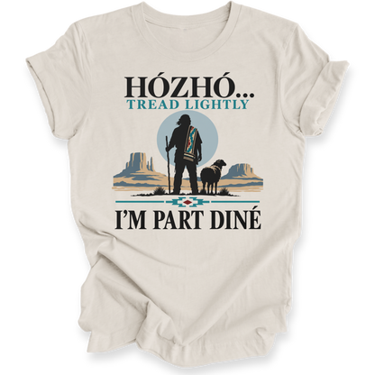 A beige short-sleeve t-shirt with a graphic print on the front. The graphic features a silhouette of a Native American standing with a staff next to a sheep, set against a desert landscape with mesas and a blue circle.