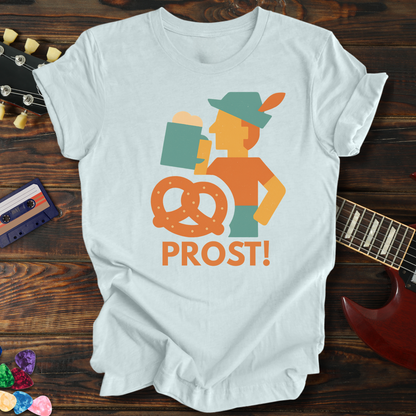 White t-shirt with 'PROST!' graphic design on a wooden surface with a guitar and cassette tape.