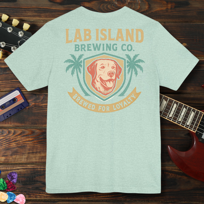 Light blue t-shirt with 'Lab Island Brewing Co.' logo on a wooden surface with a guitar and cassette tape.