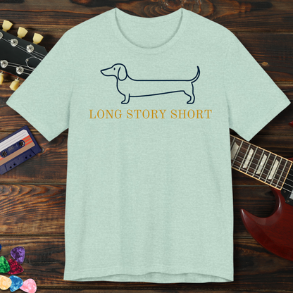 Light green t-shirt with dachshund graphic and 'Long Story Short' text on a wooden surface with guitar and cassette tape.