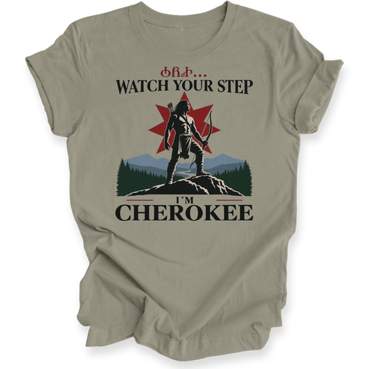 A light olive green short-sleeve t-shirt with a graphic print on the front. The graphic features a Native American figure standing on a rock with a red star and mountains in the background, with the text 'CHEROKEE.
