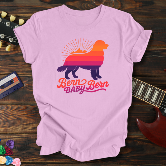 Pink t-shirt with dog graphic and text on a wooden surface with guitar and cassette tape.